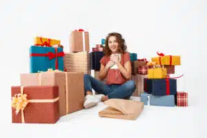 Young beautiful curly girl sitting on floor among gift boxes with just opened present tablet Isolated